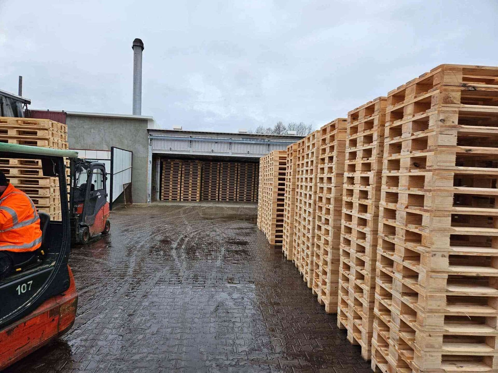 Wózek widłowy przy hali produkcyjnej obok stosów palet